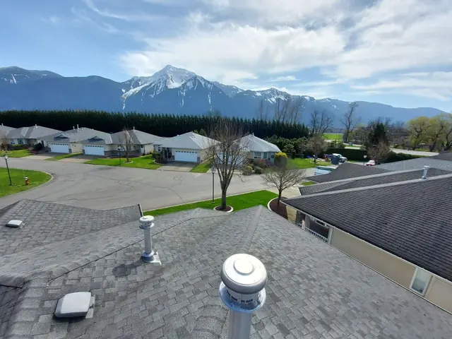 Roof tear-off in progress showing exposed yellow OSB sheathing and wooden deck structure during residential roof replacement, with mountains in scenic backdrop.