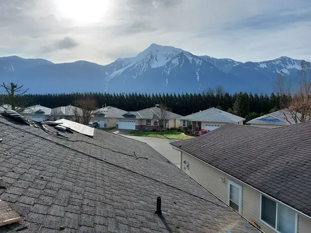 Scenic landscape view of dark gray asphalt shingle roof installation on residential property with Cascade mountain backdrop and evergreen forest, typical Chilliwack roofing project.