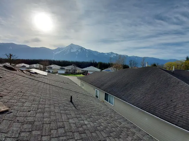 Completed dark gray asphalt shingle roof with visible roof vent penetrations, installed on residential home with mountains in background in Chilliwack area.
