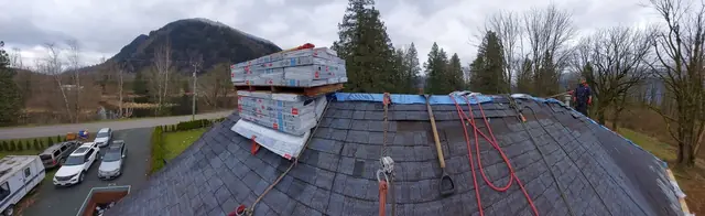 Large residential roof tear-off with blue roofing underlayment and ice shield installed, panoramic mountain backdrop visible during early project phase.