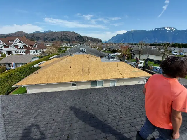 Close-up of experienced roofer working on asphalt shingle roof with mountain scenery visible, demonstrating quality roofing craftsmanship and attention to detail.