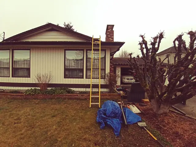 Residential roof mid-tear-off showing exposed decking after shingle removal, with blue tarping and safety equipment visible, representing the roughing phase of a complete roof replacement project.