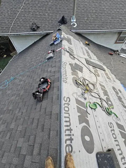 Professional roofers installing architectural asphalt shingles on a residential roof with proper safety equipment and harnesses, showing mid-installation progress on the shingle course application.