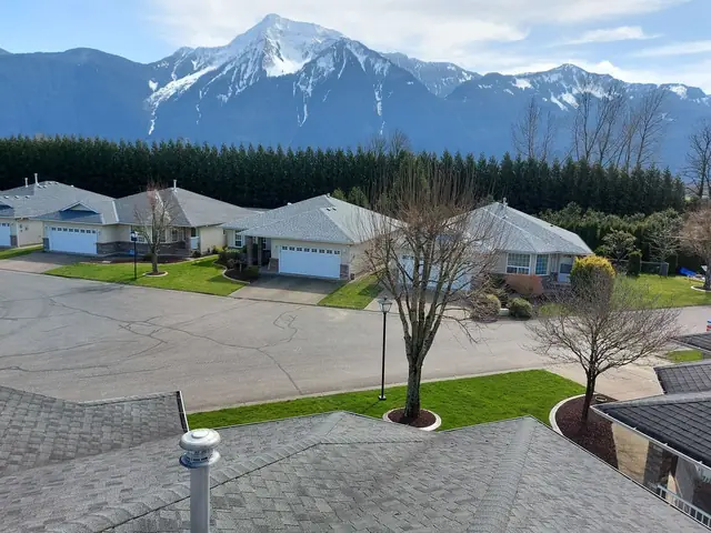 Expansive white metal standing-seam commercial roof installation with mountain peaks visible in background, typical of Fraser Valley industrial and commercial roofing projects.