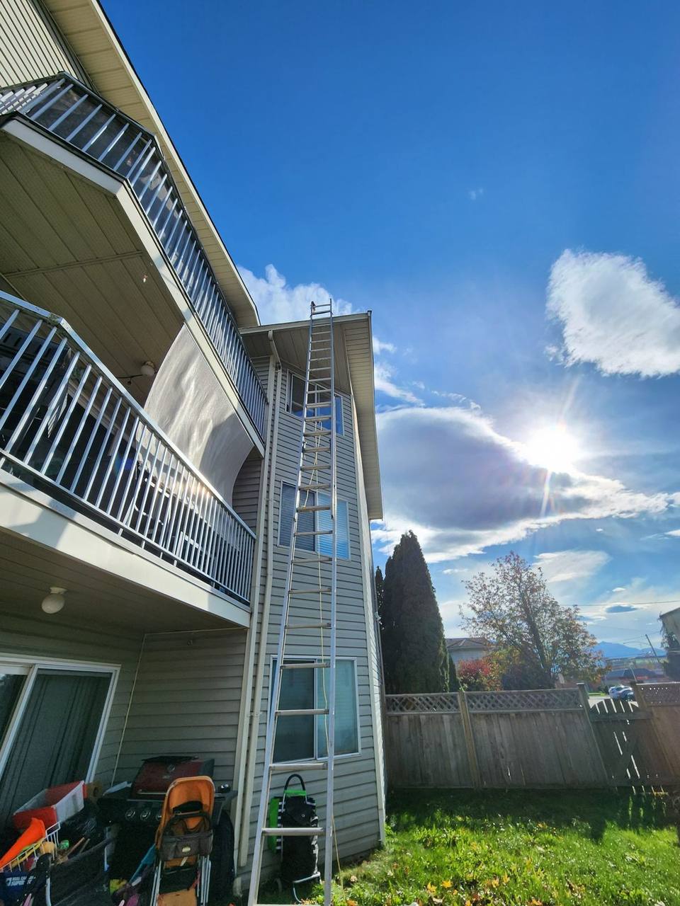 Fraser Roofing extension ladder properly positioned against a two-story Fraser Valley home, extending above the roofline for safe roof access