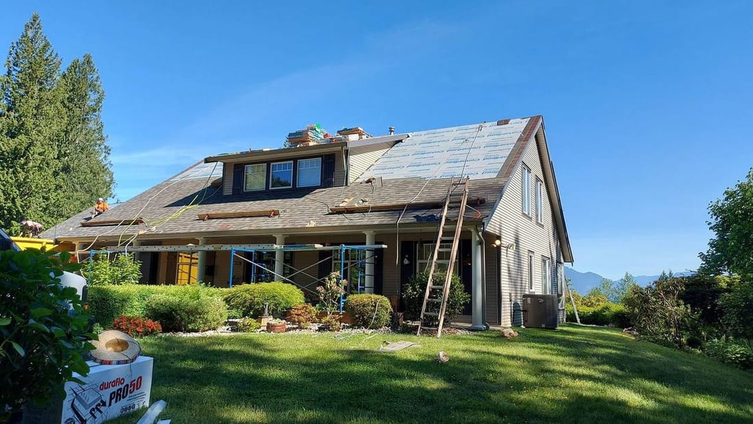 Full re-roof in progress on Chilliwack home with synthetic underlayment installed and new shingles staged on ridge