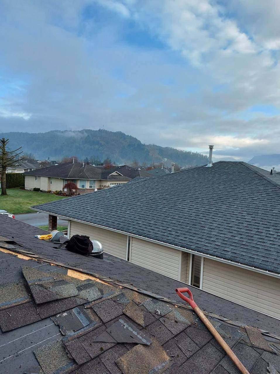 Emergency roof tear-off with old shingle removal on Fraser Valley residential home with mountains in background by Fraser Roofing