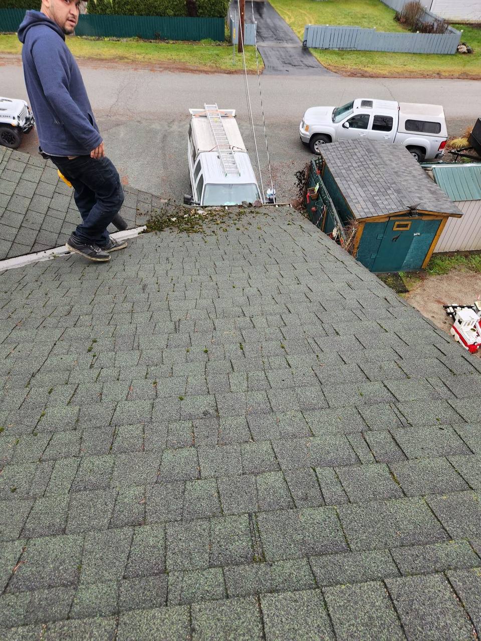 Fraser Roofing worker inspecting a residential roof with significant moss growth and debris buildup in the Fraser Valley, BC