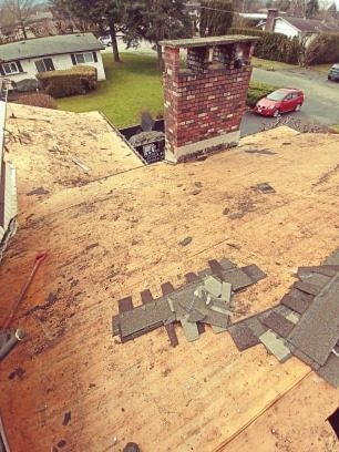 Exposed roof sheathing around brick chimney during tear-off by Fraser Roofing in the Fraser Valley