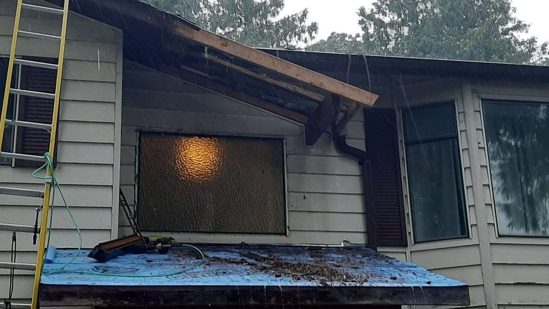 Roof replacement in progress during rainy weather showing blue underlayment and exposed sheathing in Fraser Valley
