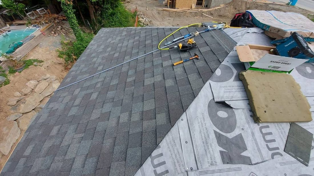Architectural asphalt shingle installation in progress on new construction roof in Rosedale BC showing completed section and professional roofing tools