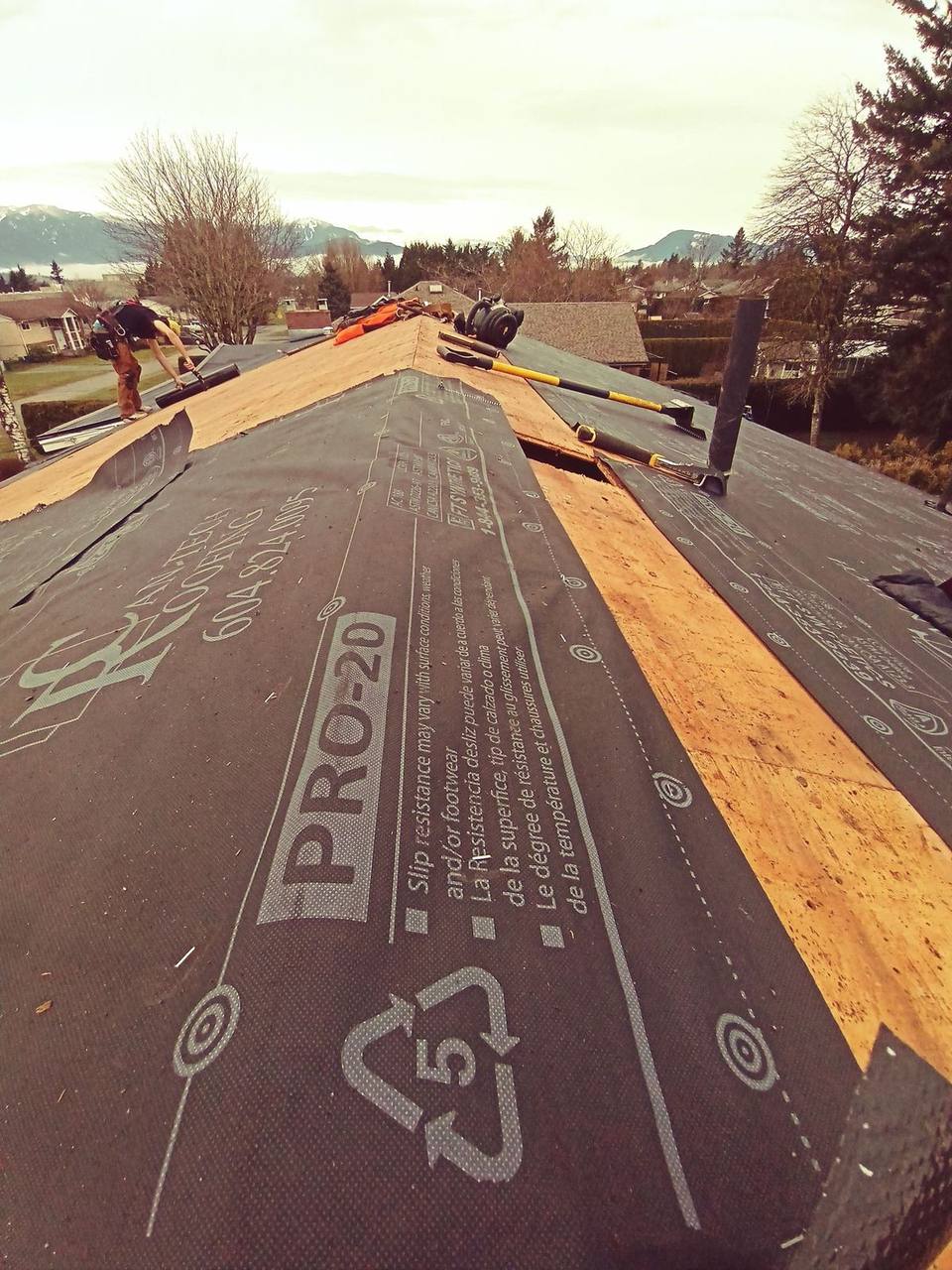 Fraser Roofing crew installing PRO-20 synthetic underlayment along roof ridge with Fraser Valley mountains in background
