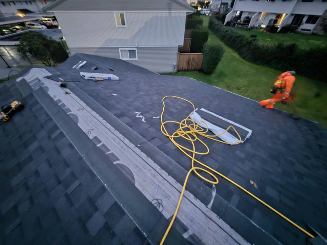 Fraser Roofing crew almost done shingling a residential roof in Chilliwack wearing rain gear, showing dedication to working in Fraser Valley weather