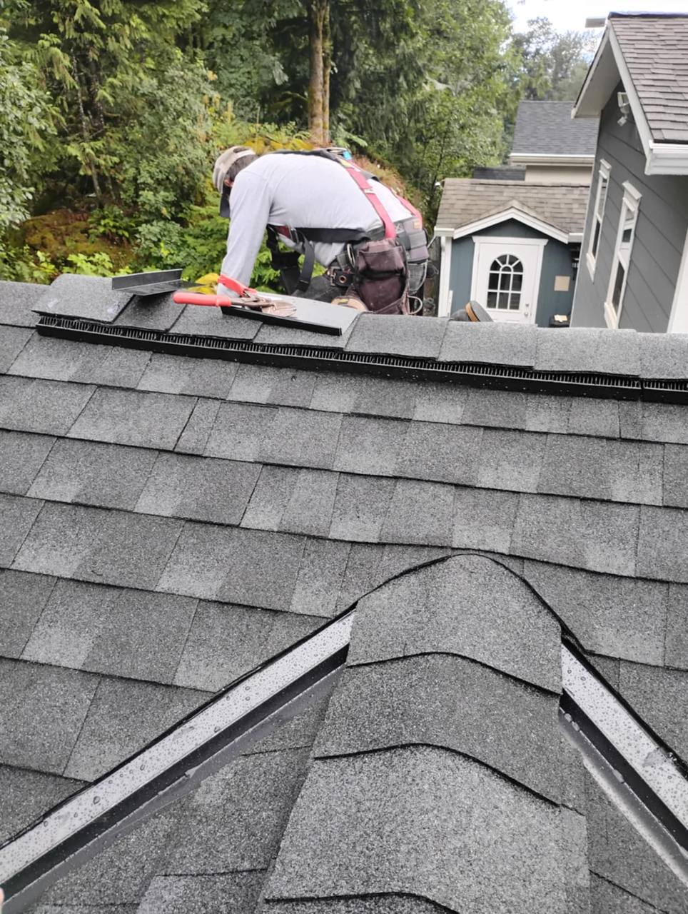Fraser Roofing crew member finishing shingling work near the ridge cap on a residential roof, showing precise craftsmanship on a Harrison area project