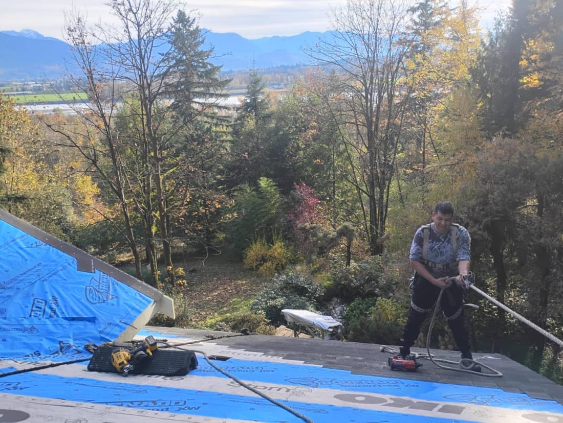 Fraser Roofing crew member working on a partially shingled residential roof in Chilliwack, showing progress mid-installation on a hillside property