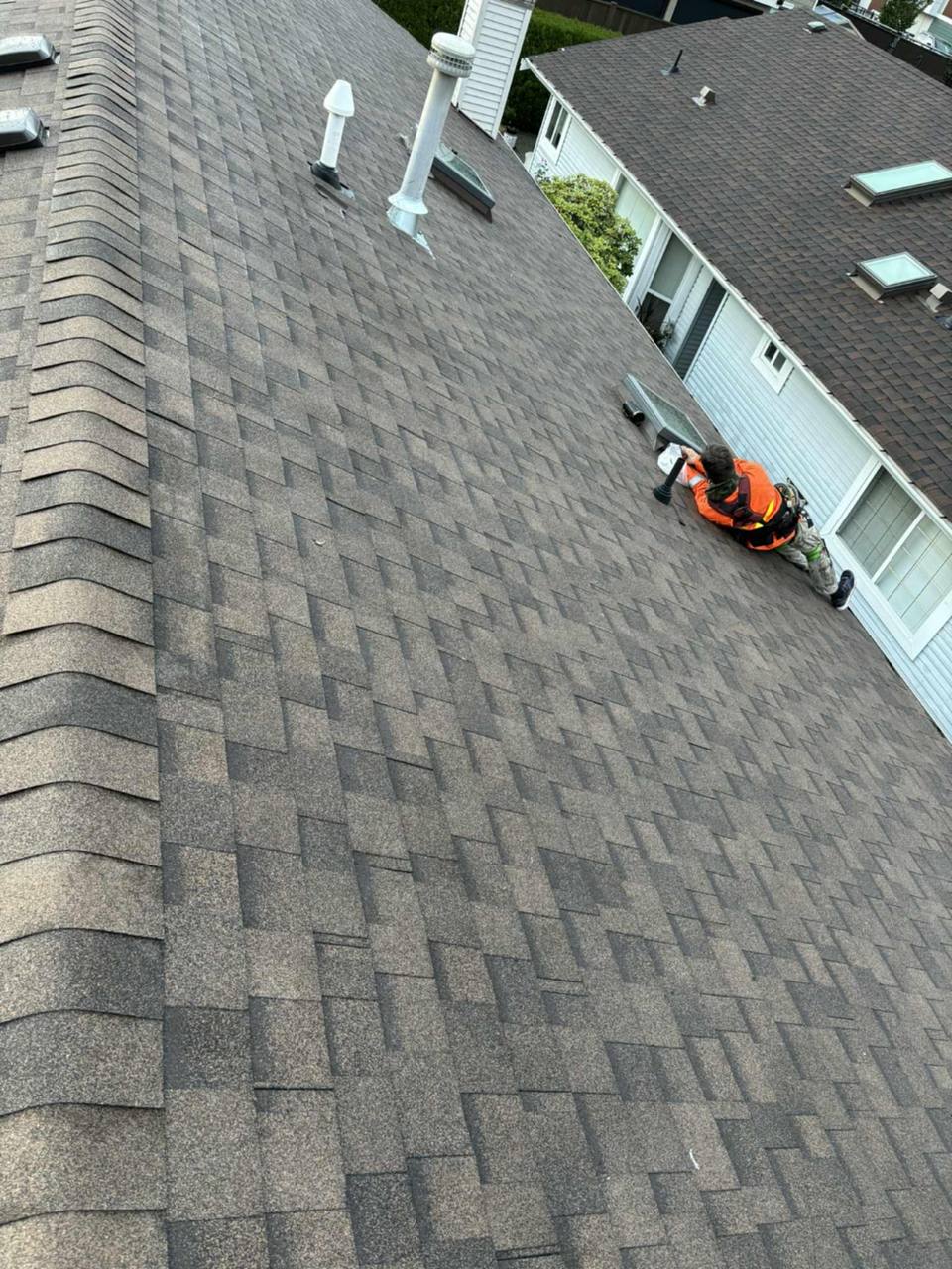 Fraser Roofing crew member sealing a skylight on a residential roof in Chilliwack, BC with Fraser Valley mountains in the background