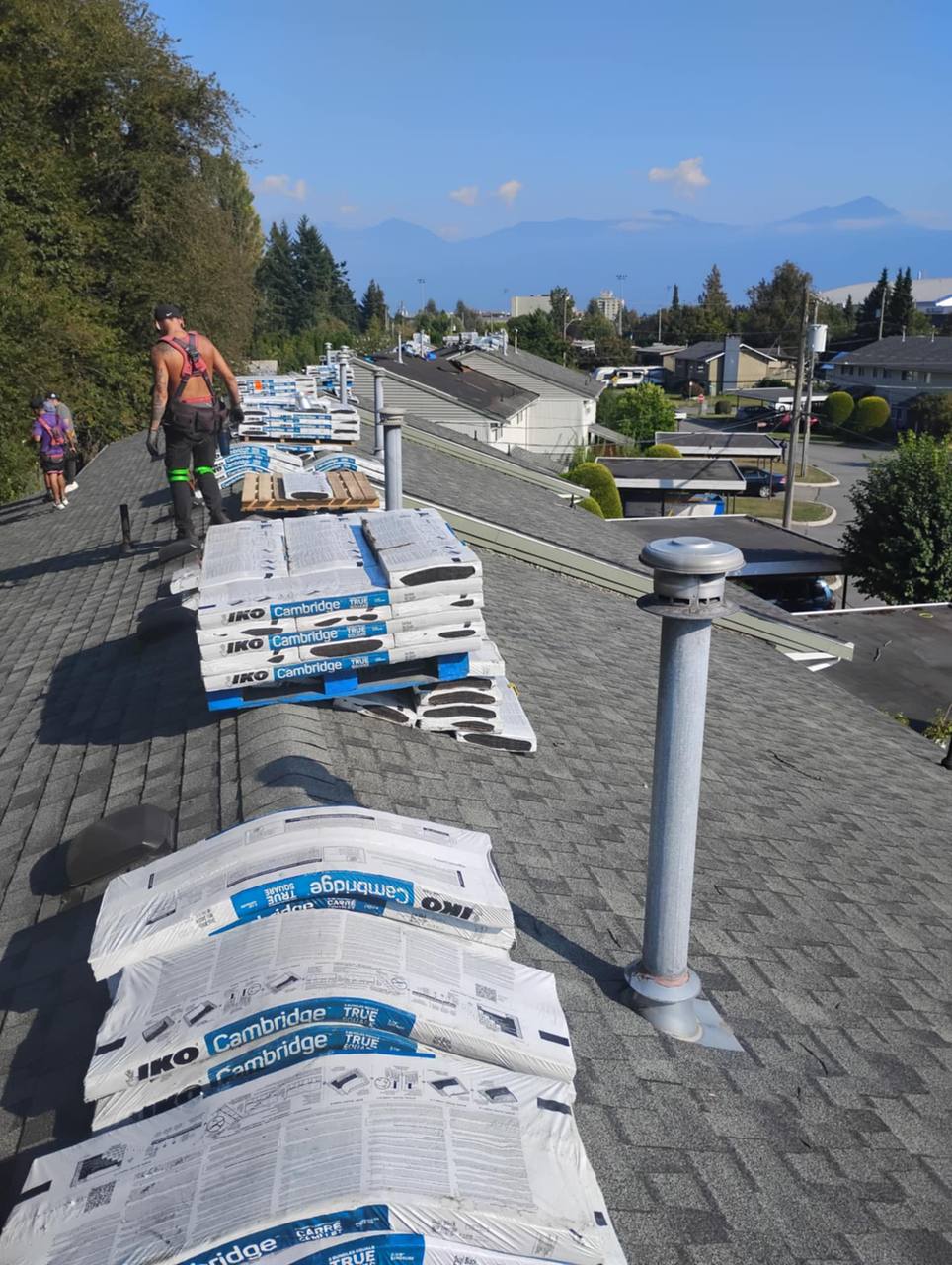 Fraser Roofing crew mid-job on a large complex Chilliwack roof with shingled bundles staged on the peak and Fraser Valley mountains in background