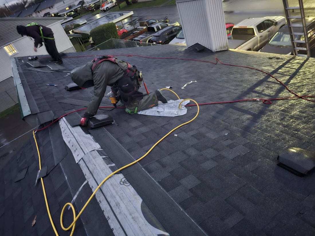 Two Fraser Roofing crew in harnesses shingling a low slope roof