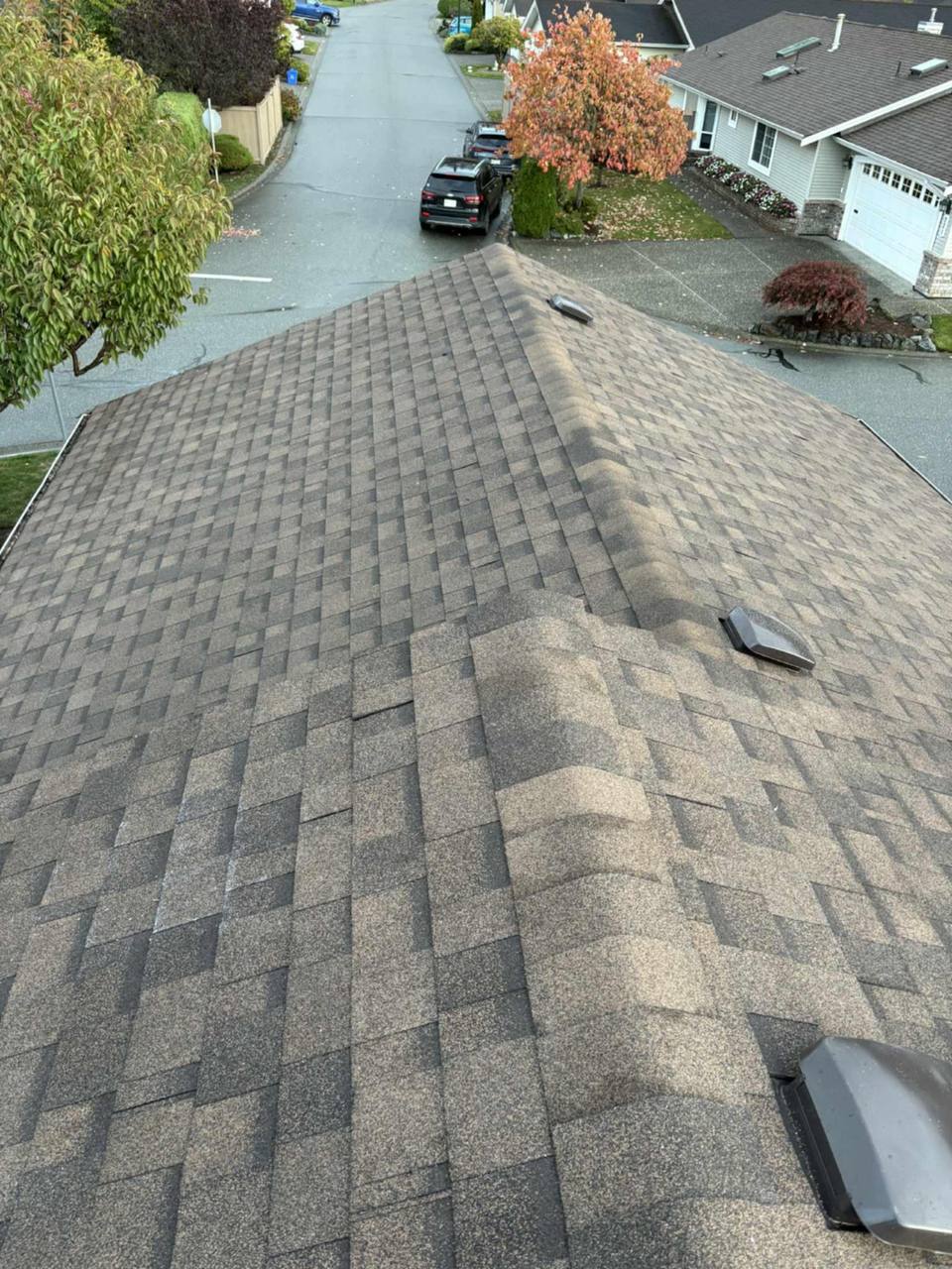 Completed asphalt shingle re-roof with ridge inspection view on a multi-plane residential home in Chilliwack neighbourhood by Fraser Roofing