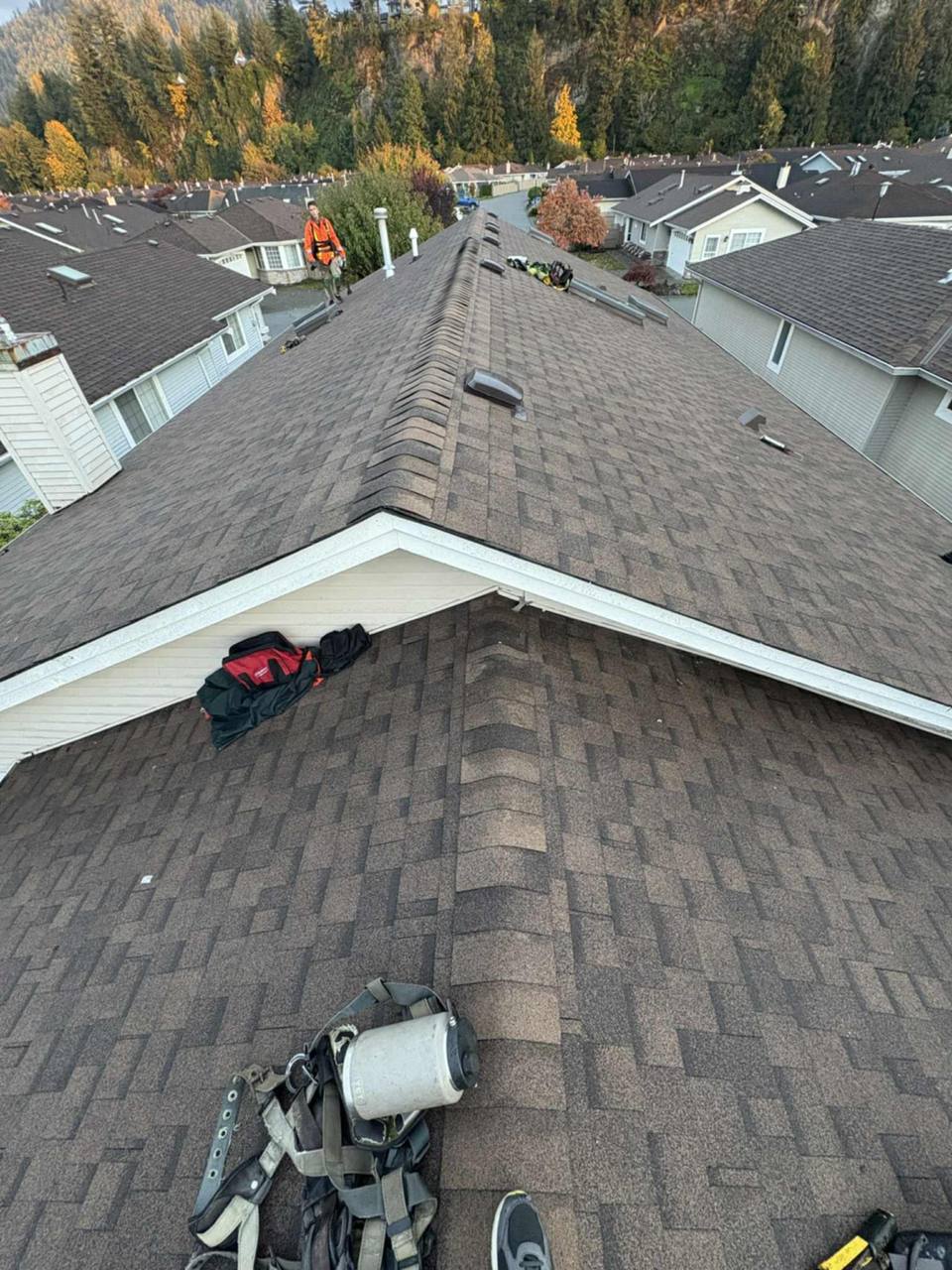 Roofer in orange hi-vis vest performing final inspection along the ridge line of a completed multi-unit residential complex in Chilliwack BC by Fraser Roofing