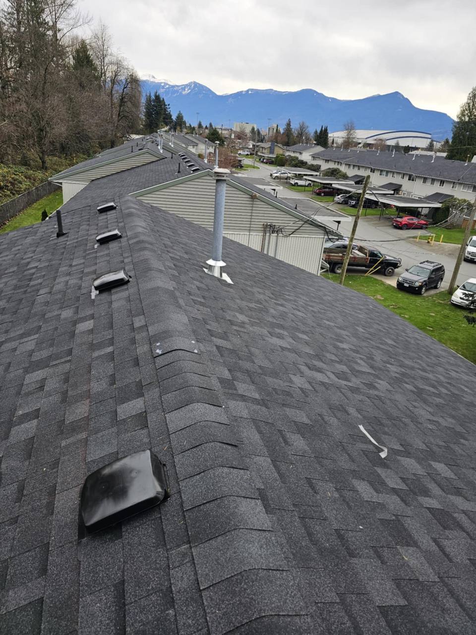 Completed dark charcoal architectural asphalt shingle reroof with ridge vents in Chilliwack BC by Fraser Roofing with Cheam Range mountains in background