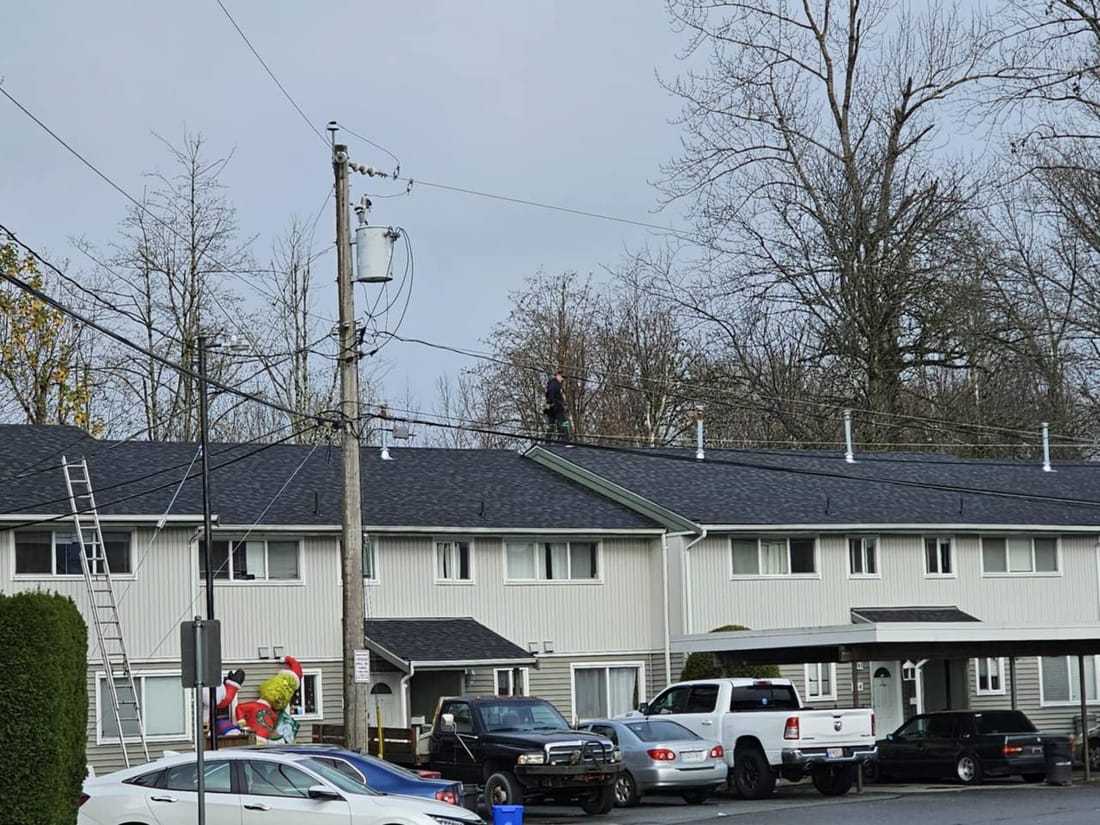 Completed strata townhouse re-roof in Chilliwack BC with roofer performing final quality inspection on dark charcoal architectural shingles by Fraser Roofing
