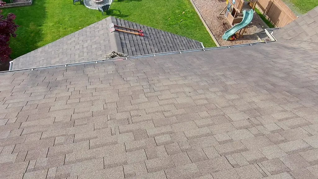 A first-person view down a roof slope toward a landscaped backyard with a trampoline, garden beds, a fire pit with chairs. Fraser Roofing