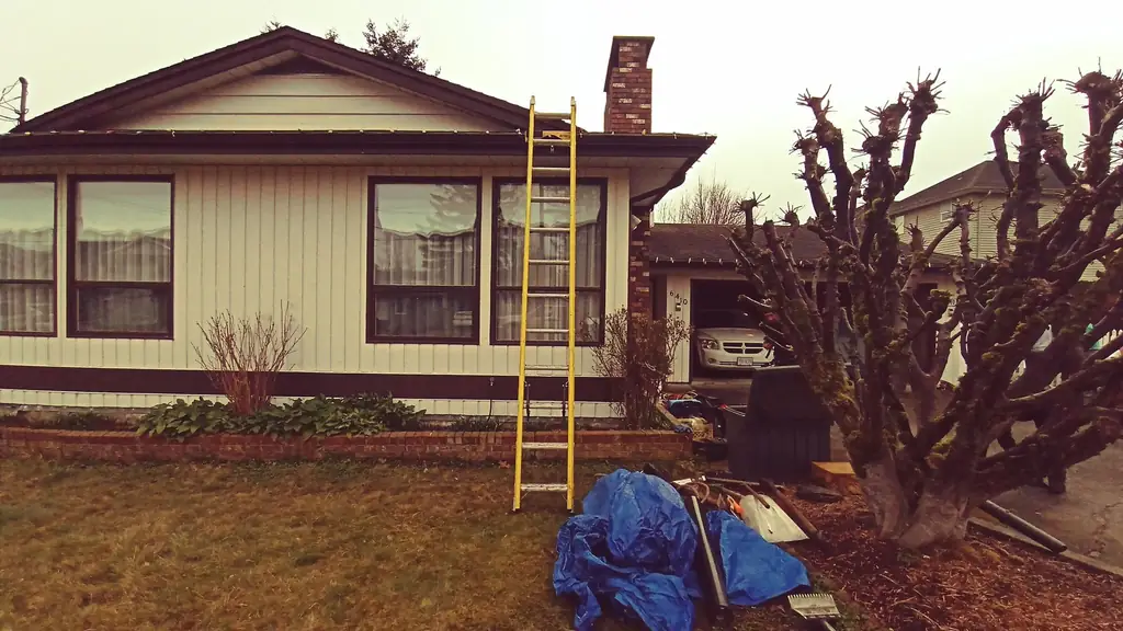 A single-story ranch-style house with cream vertical siding and a brick chimney, photographed from the front lawn on an overcast day. Fraser Roofing