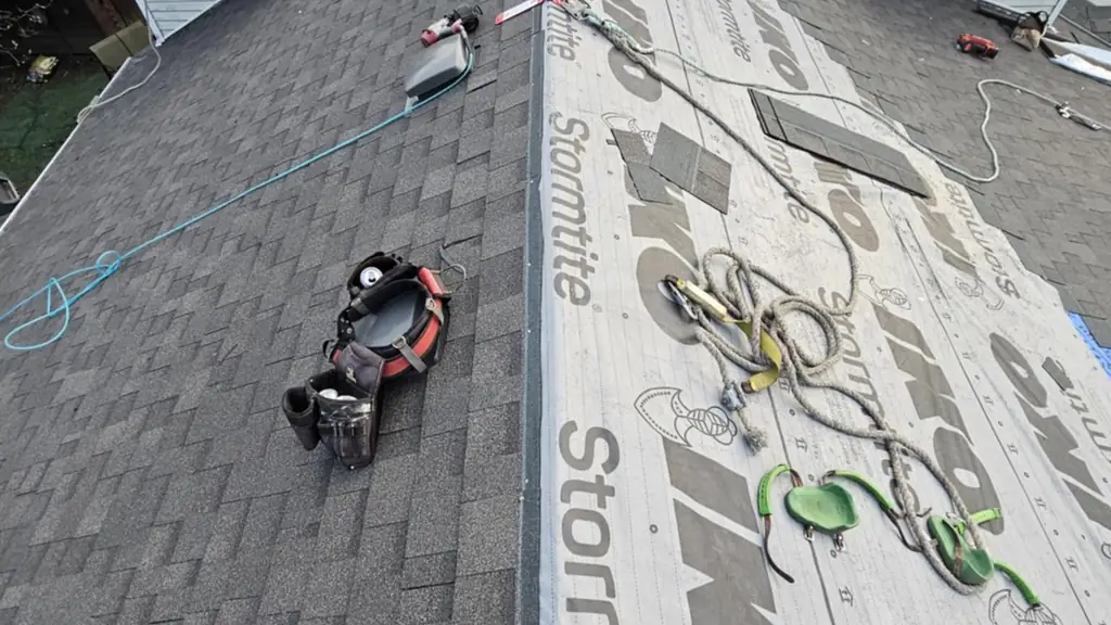 Looking down from a roof peak along two adjoining slopes: one already shingled dark grey. Fraser Roofing