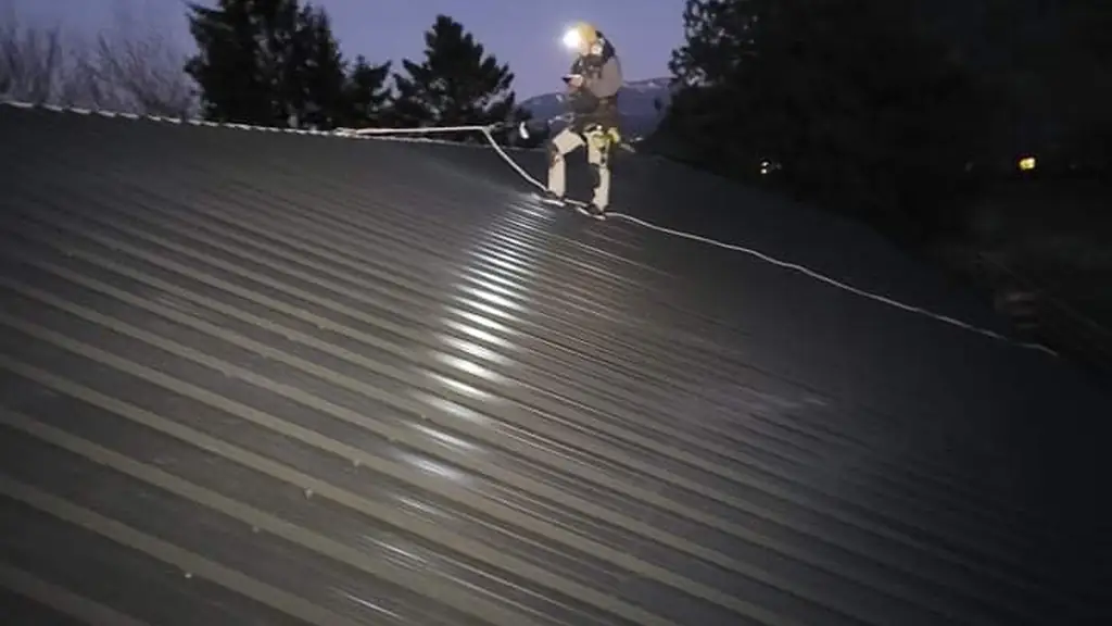A worker with a lit headlamp stands near the ridge of a corrugated metal roof at dusk. Fraser Roofing