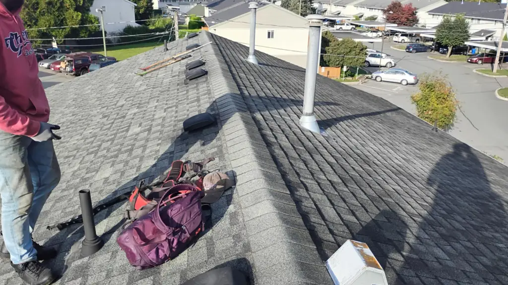 A worker in a maroon hoodie stands on a completed shingled roof, looking out over the neighbourhood. Fraser Roofing