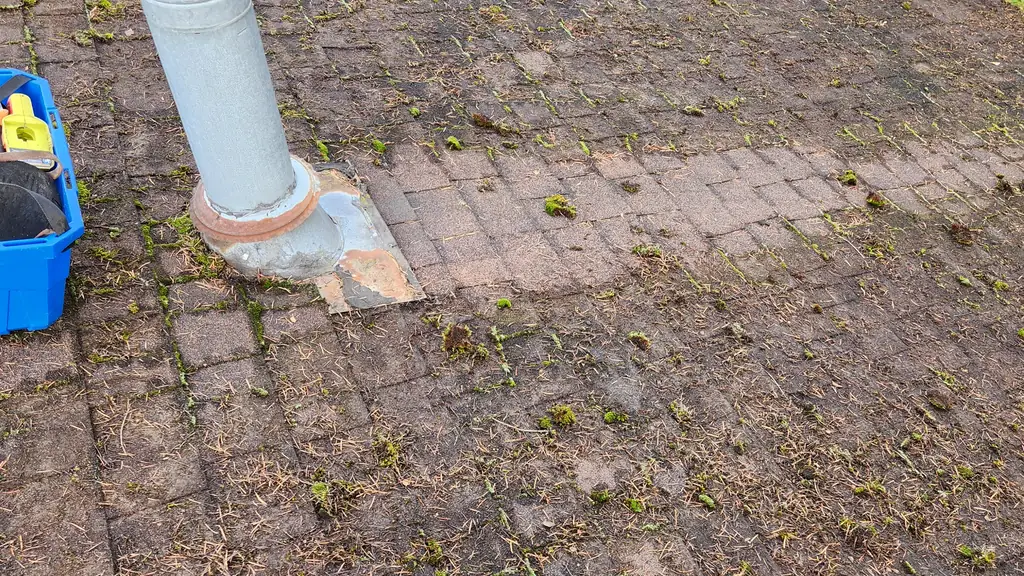 A galvanized metal plumbing vent stack with a patched, repaired flashing base rises from a dirty asphalt shingle roof sparsely flecked with moss. Fraser Roofing