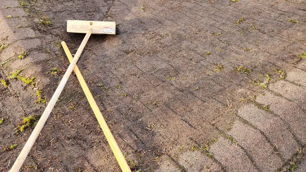 Overhead view of a dirty asphalt shingle roof valley with a roof rake and a push broom laid crossed over the shingles. Fraser Roofing