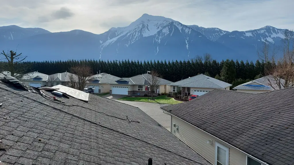 A striking view from a rooftop over a subdivision of single-story homes toward a large snow-capped mountain peak rising above a dense line. Fraser Roofing