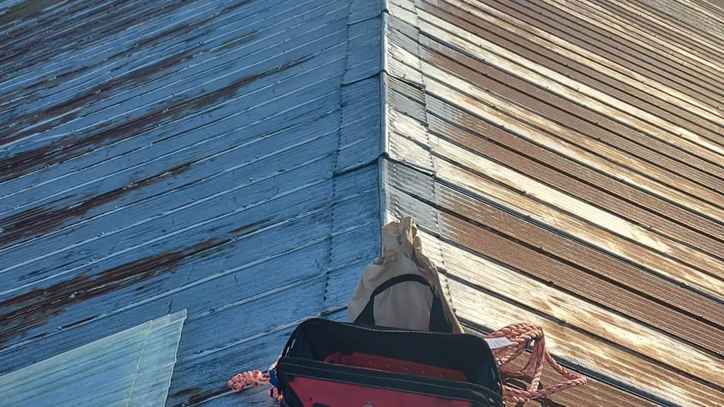 Standing on the ridge of an old, visibly rusted corrugated metal barn roof, not a new standing-seam installation as the filename suggests. Fraser Roofing