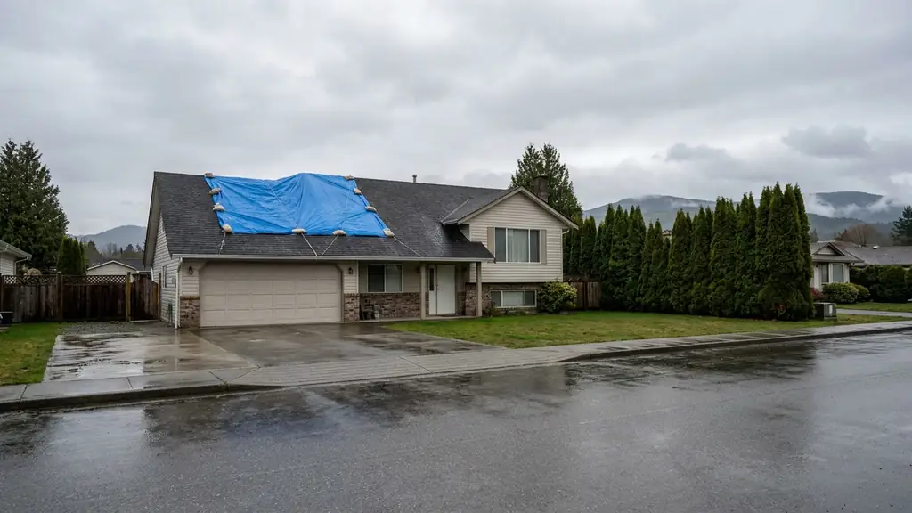 House with a blue emergency tarp over part of its roof after a storm in the Fraser Valley. Fraser Roofing