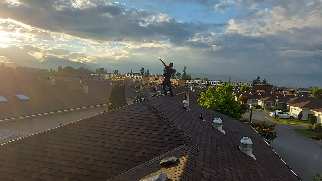 A dramatic wide sky shot over a residential neighbourhood at low sun, with a worker silhouetted near a ridge. Fraser Roofing