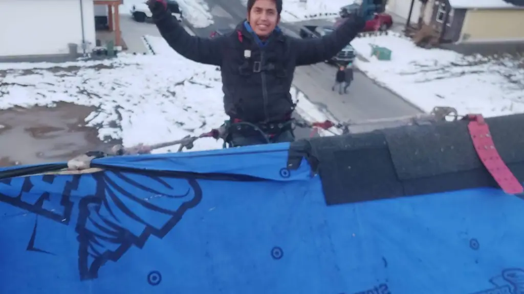 A worker throws both arms up in celebration on a snow-covered roof ridge, his face visible and smiling. Fraser Roofing