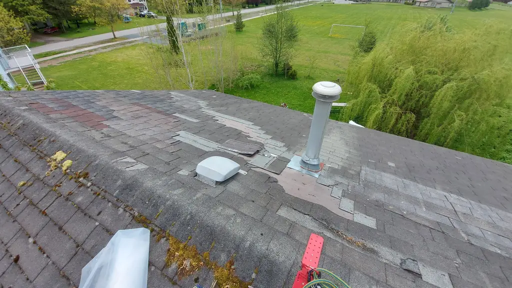 A worn, moss- and lichen-covered old asphalt shingle roof with shingles pulled up around a plumbing vent stack and a roof vent. Fraser Roofing