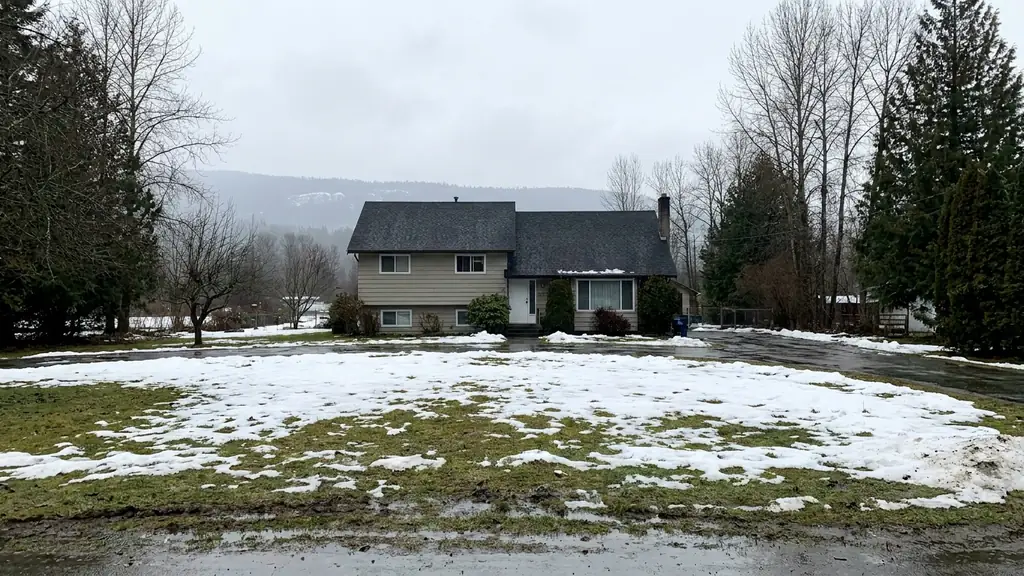 House with a dark shingle roof on a wet winter day with melting snow on the lawn. Fraser Roofing
