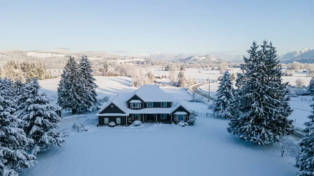 Two-storey house with fresh snow covering its roof on a clear winter morning. Fraser Roofing