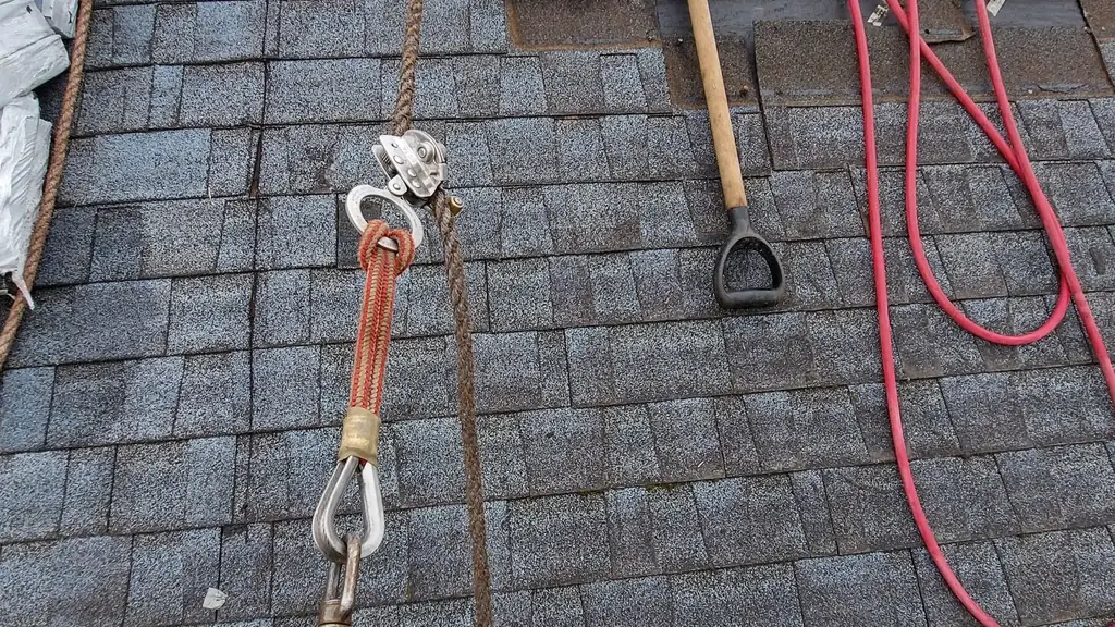 A close-up on a roof of a fall-protection rope and pulley/carabiner rig clipped to a person's harness. Fraser Roofing