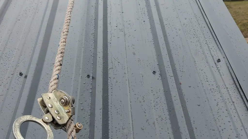 Close view of a wet gray standing-seam metal roof panel with visible rain droplets across its surface. Fraser Roofing