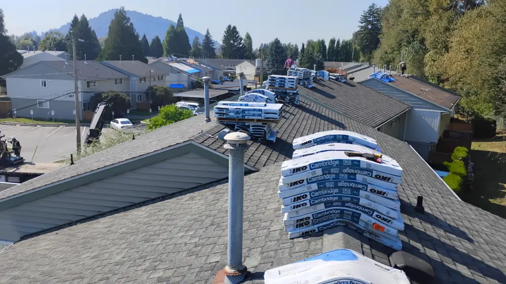 Overhead view down a long ridge stacked with IKO Cambridge shingle bundles and a bundle of IKO Leading Edge Plus starter strip. Fraser Roofing