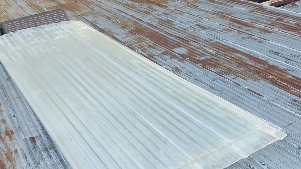 Close view of old rusted corrugated metal roof panels being removed from a barn, with one section pulled up to expose the wooden rafters underneath. Fraser Roofing