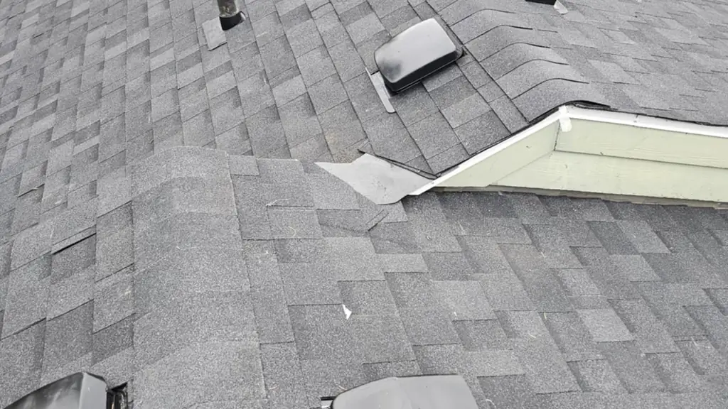 A long view along a grey asphalt shingle roof ridge with multiple black box roof vents and a plumbing stack. Fraser Roofing