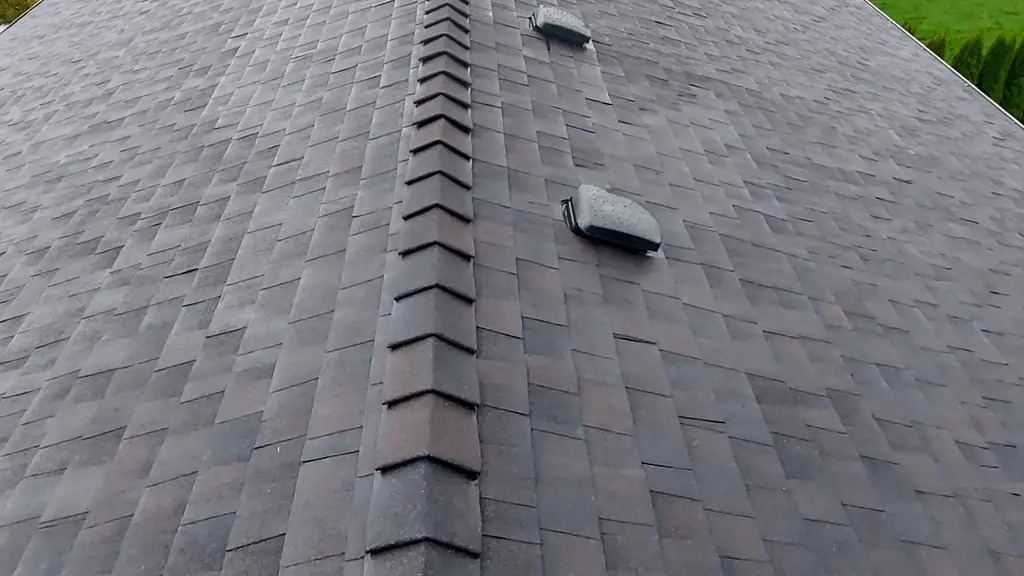 Standing on the ridge cap of a gray/brown dimensional shingle roof on a rainy, overcast day. Fraser Roofing