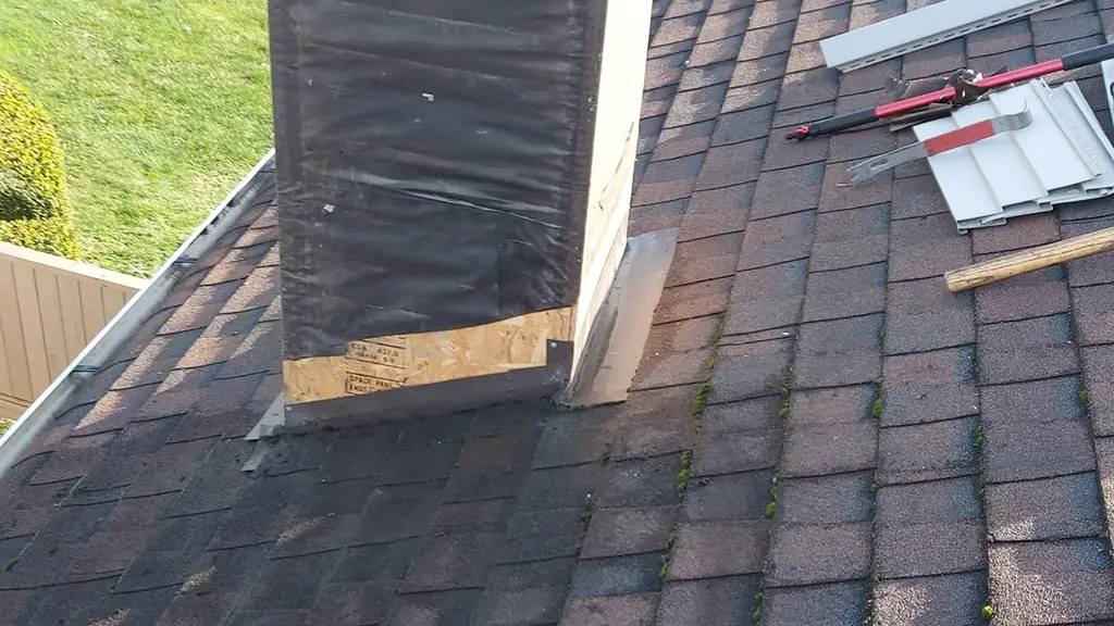 Close view of a large square metal-capped chimney chase wrapped in black underlayment at its base. Fraser Roofing
