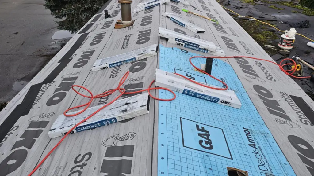 Long roof run split between IKO Stormtite underlayment and blue GAF Deck-Armor synthetic underlayment with a square cut-out hole in it. Fraser Roofing