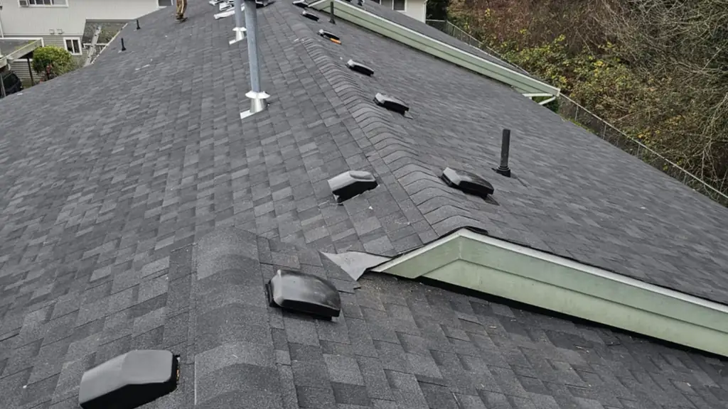 A grey shingle roof mid-installation, shot from on the roof, showing several new plastic pipe boot vents installed along the ridge and a skylight. Fraser Roofing